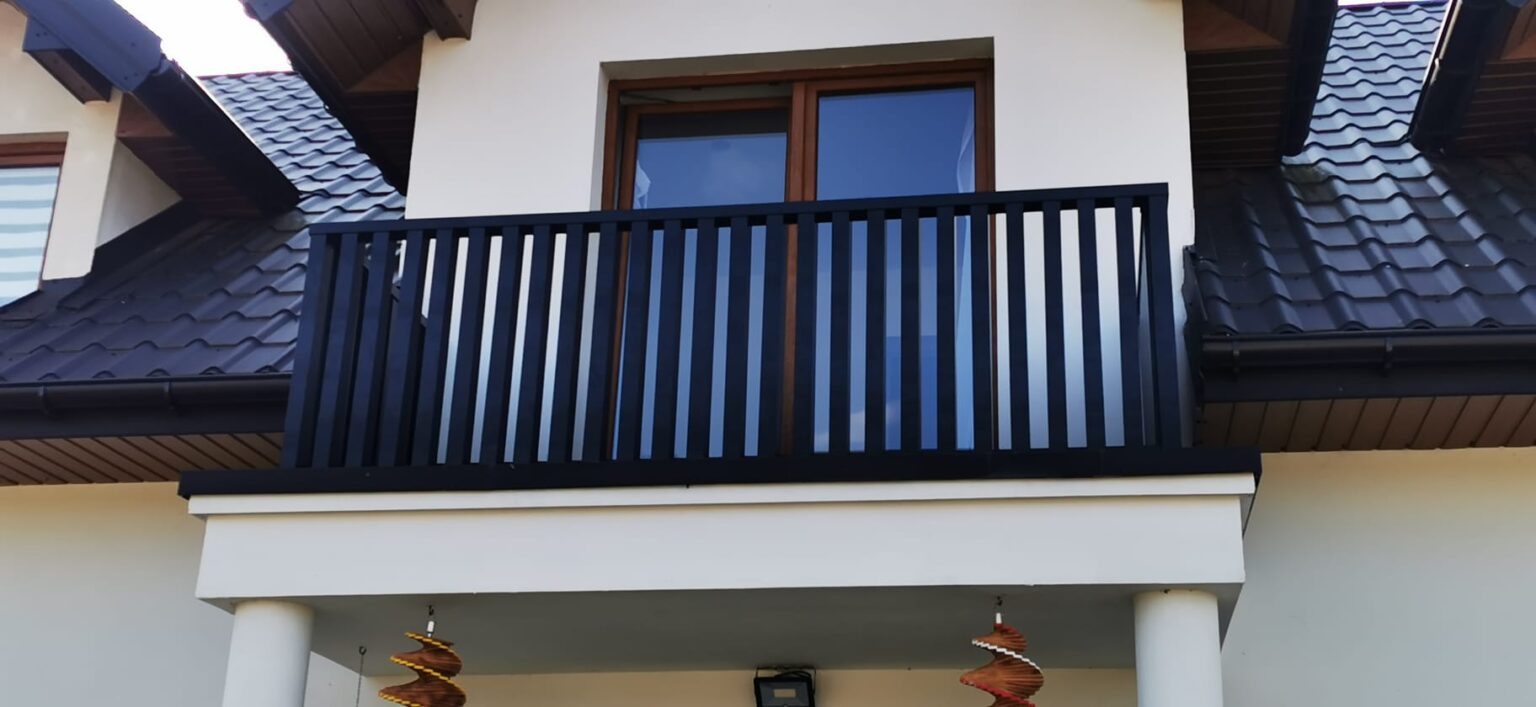 widok na balkon oraz aluminiowa balustradę o pionowych profilach. W tle elewacja budynku