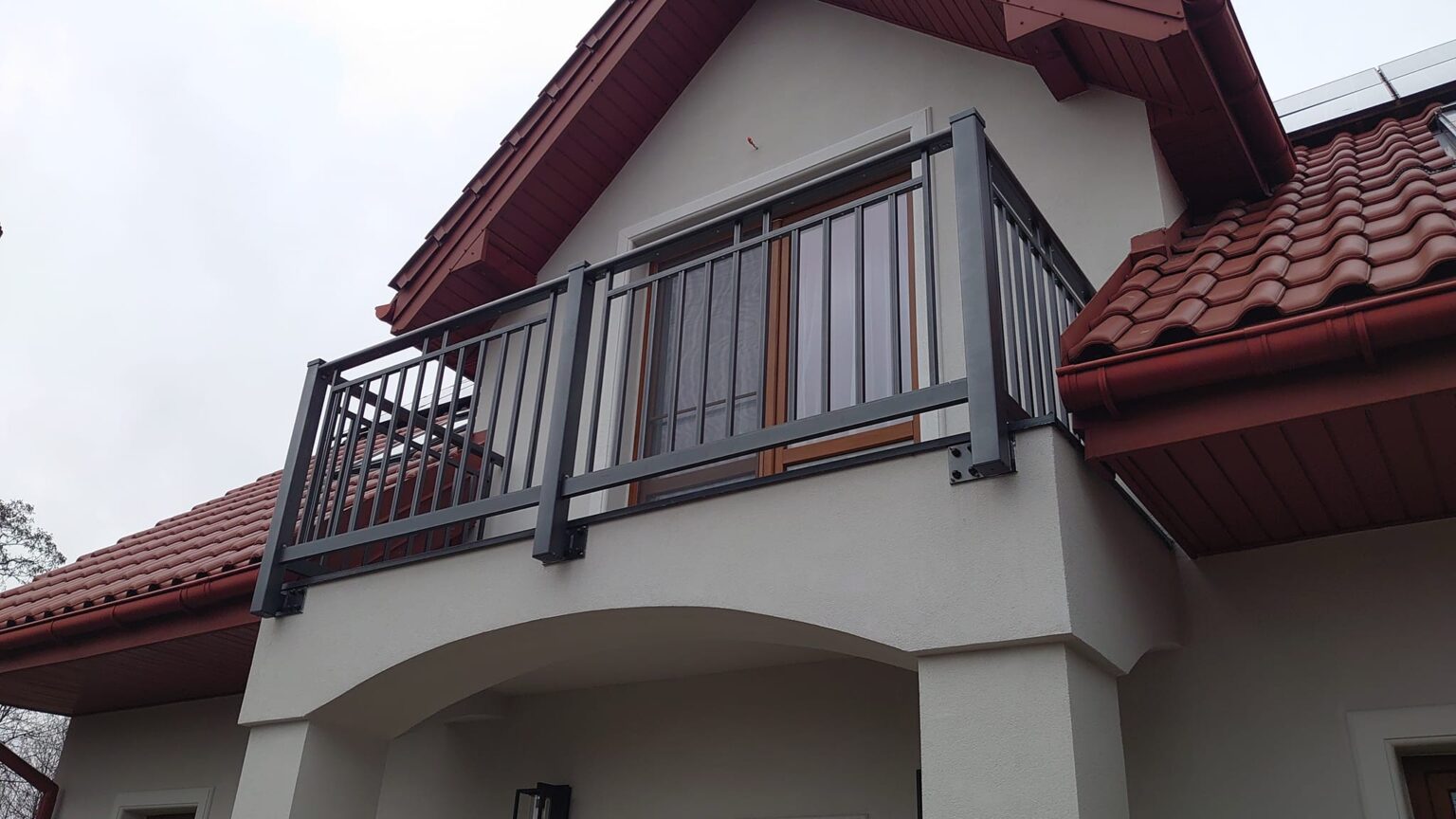 Elewacja budynku z balkonem i dachem, na pierwszym planie aluminiowa balustrada balkonowa z pionowymi profilami, model Sunny Euro Fences